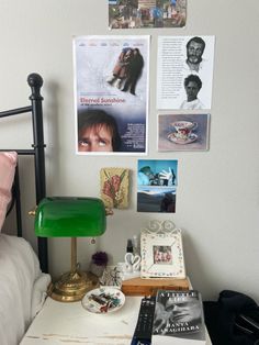 a green lamp sitting on top of a white table next to a bed with pictures above it