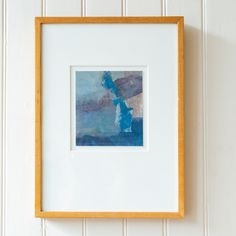 a painting hanging on the wall with a wooden frame and white walls in the background