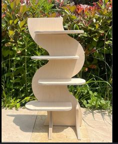 three tiered wooden shelf sitting in front of some bushes