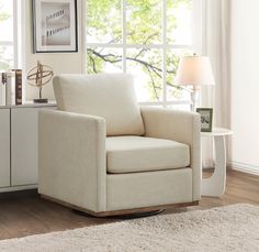 a white chair sitting in front of a window next to a table with a lamp on it