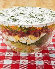 a layered salad in a glass dish on a red and white checkered tablecloth