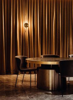 an elegant dining table and chairs in front of a curtained wall with gold drapes