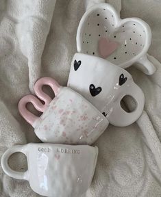 three coffee mugs sitting on top of a white blanket next to each other with hearts