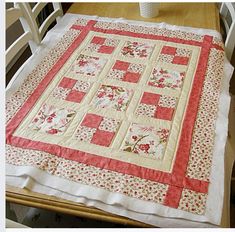 a quilted table runner on top of a wooden table with white chairs and a vase