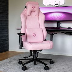 a pink gaming chair sitting in front of a computer desk with a monitor on it