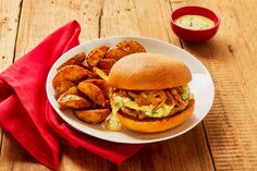 a white plate topped with a pulled pork sandwich and french fries next to a bowl of dipping sauce