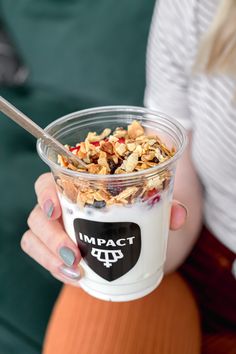 a woman is holding a cup of granola with yogurt and cereal in it