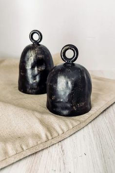 two black bell shaped objects sitting on top of a cloth covered tablecloth next to a white wall