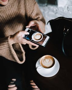 a woman sitting at a table with a cup of coffee and cell phone in her hand