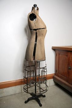 a mannequin is sitting on a stand in front of a white wall and wooden cabinet