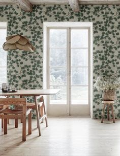 a dining room with green wallpaper and wooden table in front of two large windows