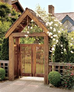 an open wooden gate with white roses growing on the top and bottom, in front of a house