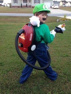 a young boy dressed up as luigi from mario kart is holding a vacuum cleaner