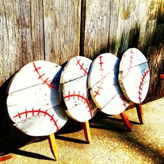 three baseballs are lined up against a wooden fence and one is painted white with red stitches