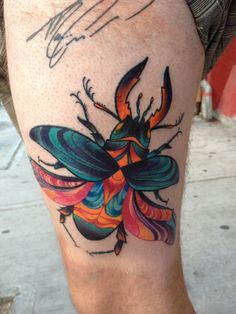 a tattoo on the leg of a man with a colorful bug design in it's center