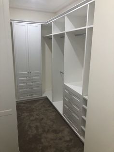 an empty walk in closet with white cabinets and drawers on the wall, carpeted floor