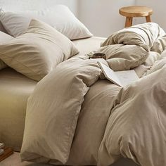 an unmade bed with several pillows on top of it and a wooden table in the background