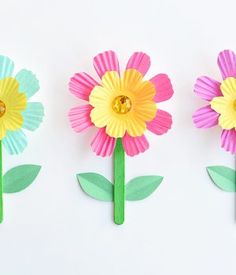 three paper flowers with green stems and yellow centers, one pink flower is on the other side