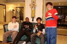 three young men sitting on a couch in front of a christmas tree