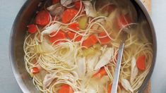 a pot filled with chicken noodle soup on top of a wooden table next to a spoon