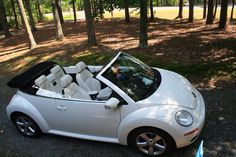 a white convertible car parked on the side of a road in front of some trees