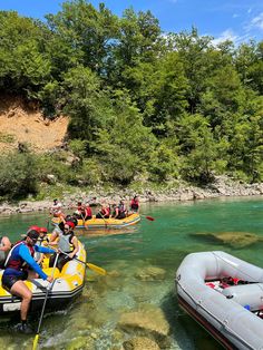 several people are rafting on the water near some rocks and trees, while another person is in an inflatable boat