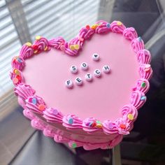 a pink heart shaped cake with words spelled on it