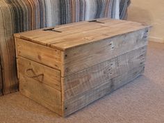 a wooden box sitting on top of a floor next to a striped couch and pillow