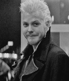 a black and white photo of a man with blonde hair wearing a leather jacket smiling at the camera