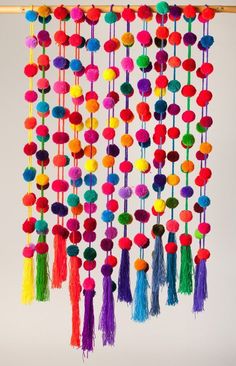 multicolored pom - poms hanging from a bamboo frame on the wall