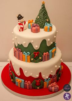 a three tiered cake decorated with presents and a snowman sitting on top of it