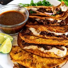 some tacos are sitting on a plate next to a bowl of sauce and lime wedges