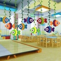 a room filled with lots of tables and chairs under colorful fish hanging from the ceiling