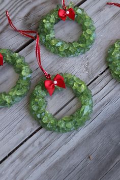 three christmas wreath ornaments with red bows hanging from them on a wooden table next to candy canes