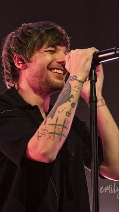 a man with tattoos on his arm singing into a microphone and smiling at the camera