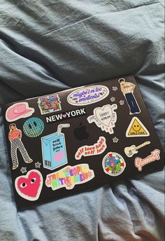 a laptop covered in stickers sitting on top of a gray bed sheet with the words new york written across it