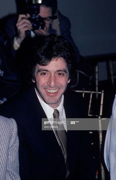 a smiling man in a suit and tie sitting next to other people with cameras around him