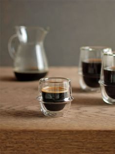 three glasses of coffee sit on a wooden table