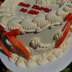 a heart shaped cake with white frosting and red bows on it's edges