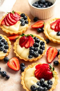 small tarts with strawberries and blueberries on them next to a bowl of yogurt