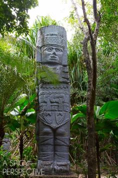 a large statue in the middle of some trees and plants with words above it that says,