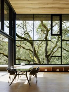 a dining room with wooden floors and large windows overlooking the trees in the forest outside