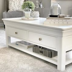 a white coffee table with two drawers on each side and a shelf below it that holds magazines