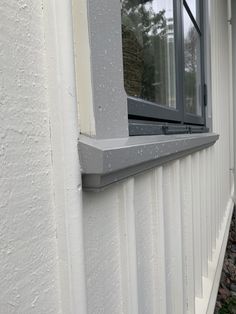 a window on the side of a house with white siding and wood trimmings