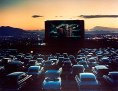 an outdoor movie screen in the middle of a parking lot with cars parked around it