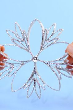 two hands are holding a silver brooch with sparkling petals on it, against a blue background