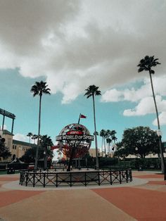 a large globe sits in the middle of a park with palm trees and buildings behind it