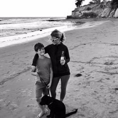 black and white photograph of two people on the beach with a dog, one holding a beer