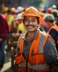 a man in an orange safety vest and hard hat smiles at the camera while other people stand around him