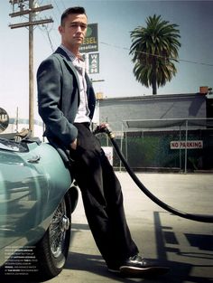 a man is sitting on the hood of a car with a gas pump in his hand